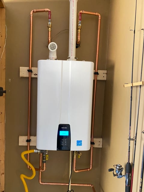 Tankless water heater mounted on wall with copper piping connections and digital display panel