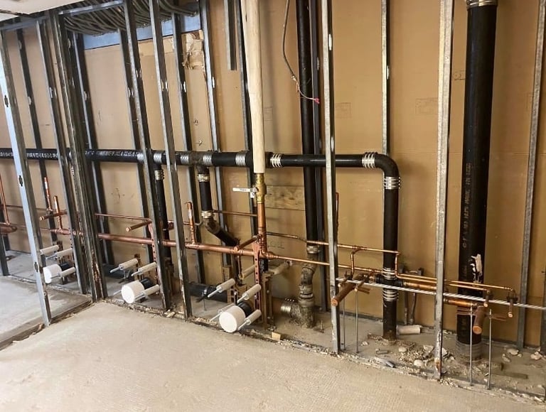 Construction site interior with metal framing, copper piping, and drywall installation in progress