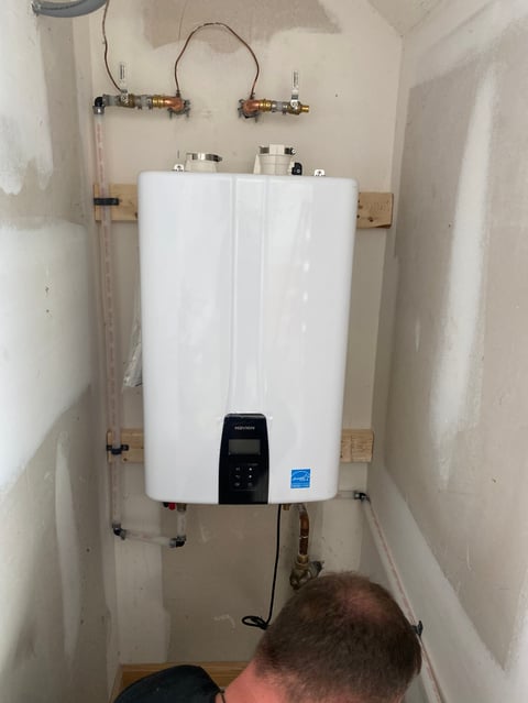 Newly installed white electric tankless water heater mounted on utility room wall with copper piping and black control panel visible